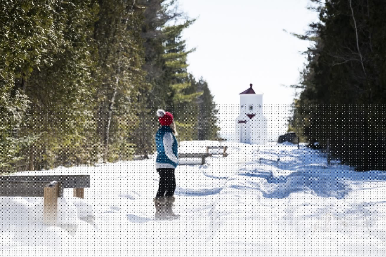 A woman standing on a snowy path leading t a white structure in the distance.